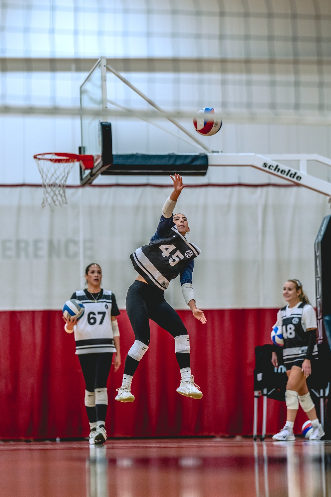 A player in a black top reaches overhead for the ball.
