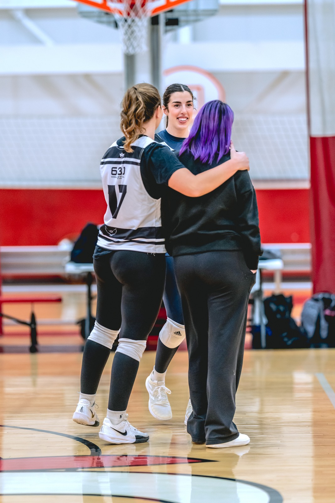 Volleyball players embrace beside an indoor court.