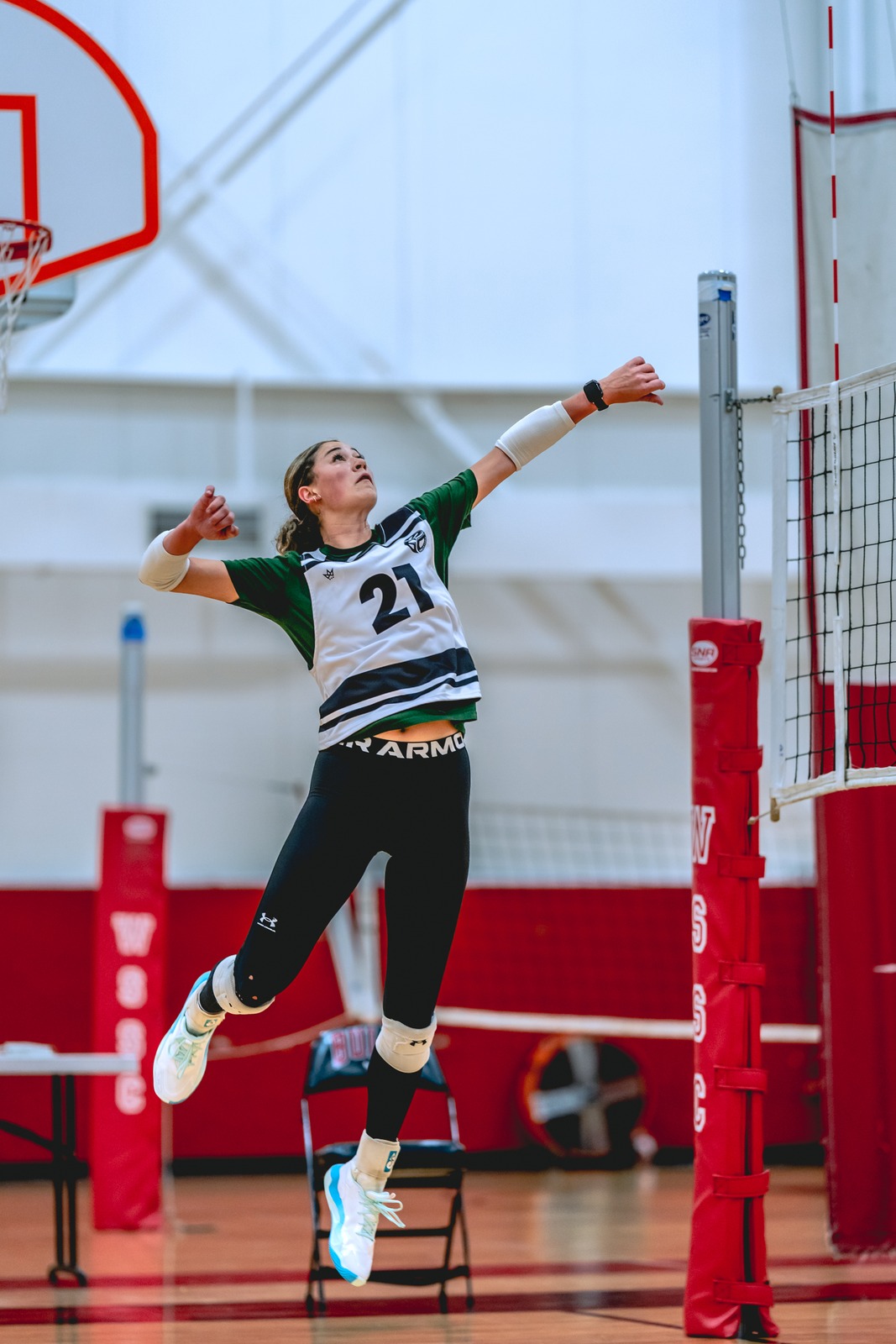 A player in a white and green top jumps with arms extended.