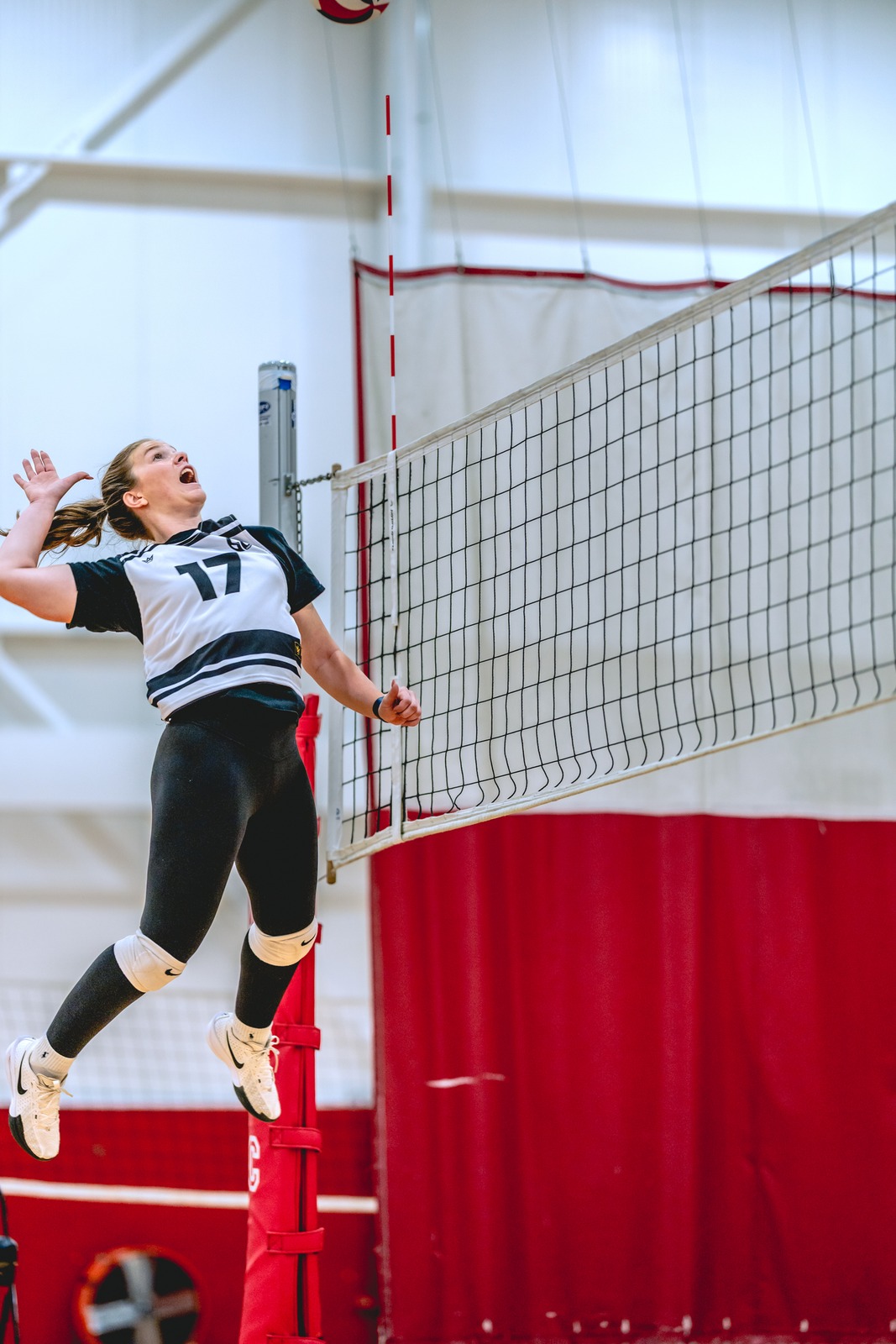 A player in a black and white top jumps with arms raised near a volleyball net.