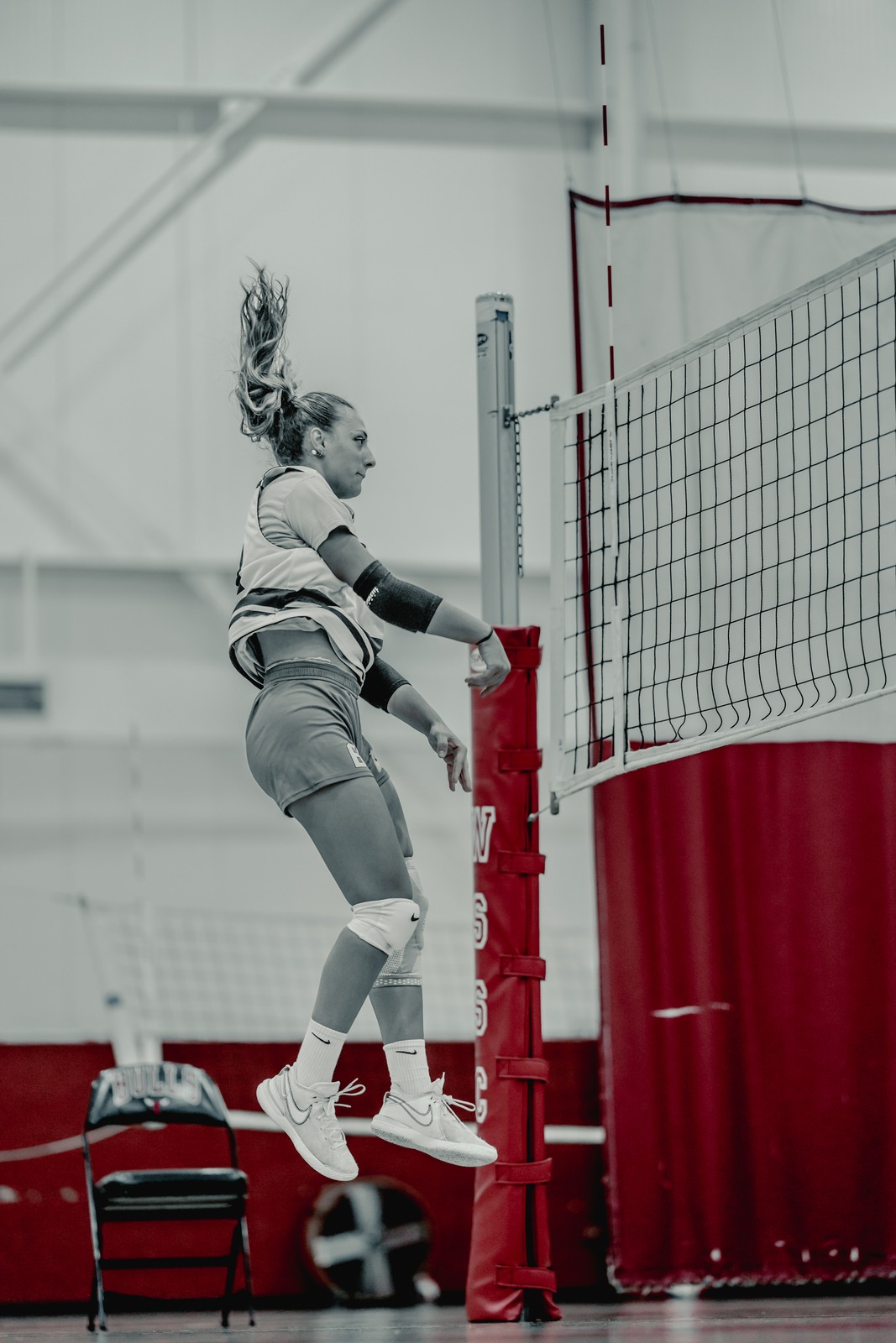 A volleyball player jumps beside the net with one arm extended overhead.
