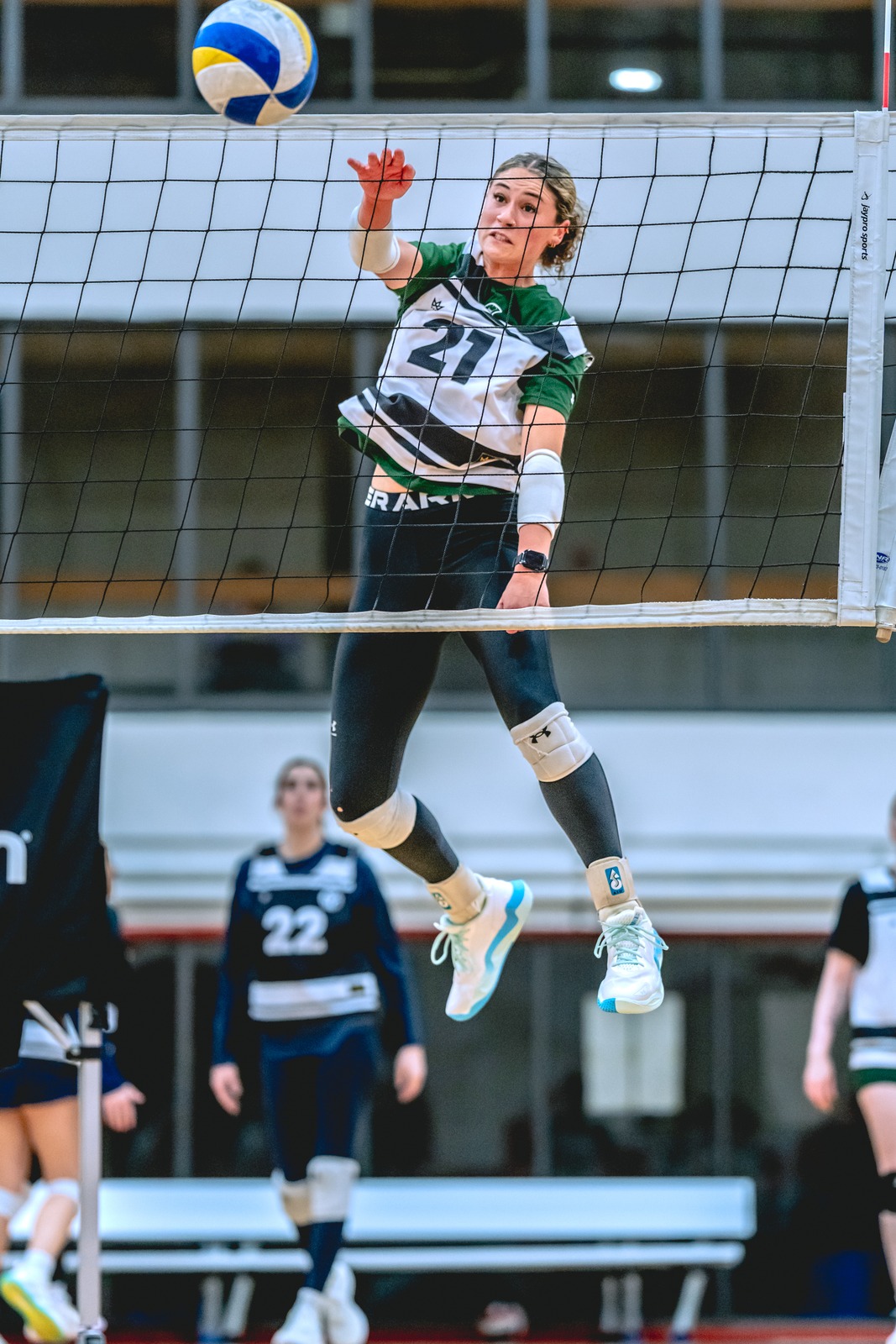 A player in a green and white top jumps near the net, reaching for the ball.
