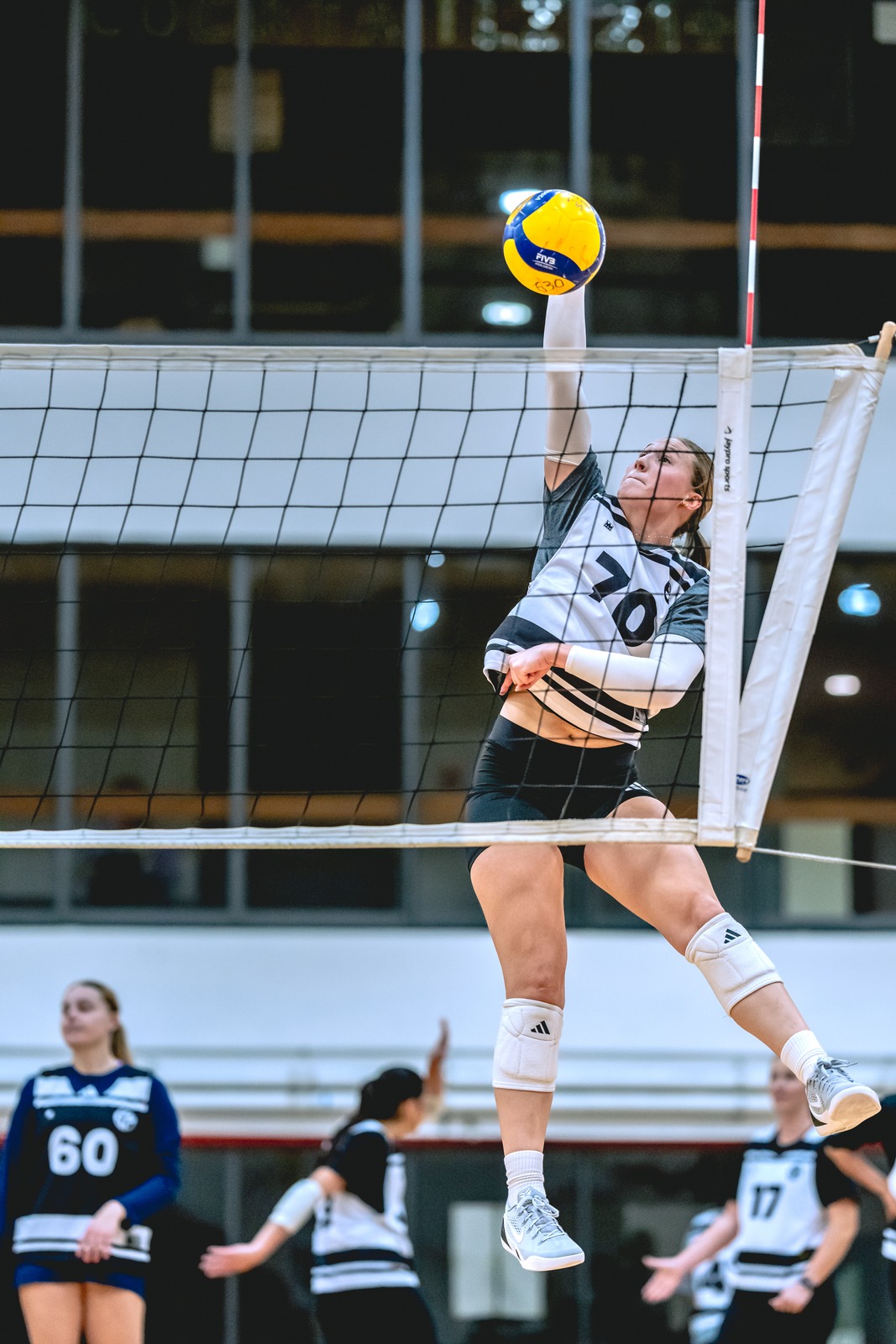A player in a black and white top reaches overhead for the ball.