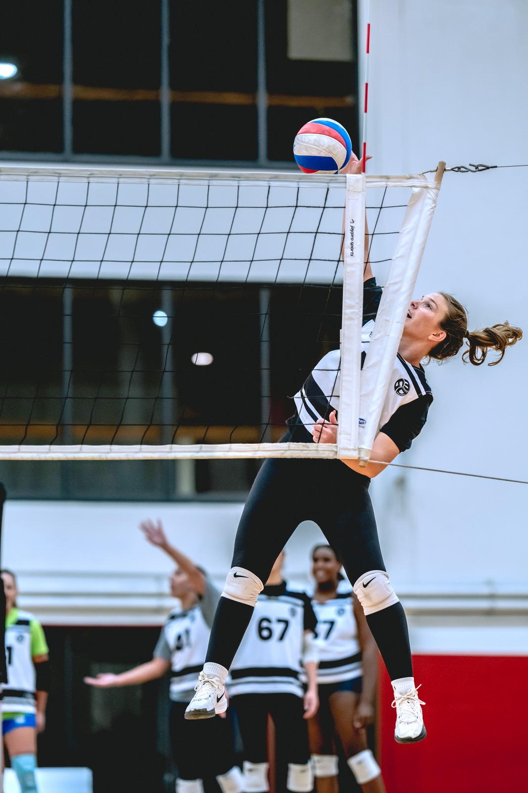A player in black and white reaches overhead for the ball.