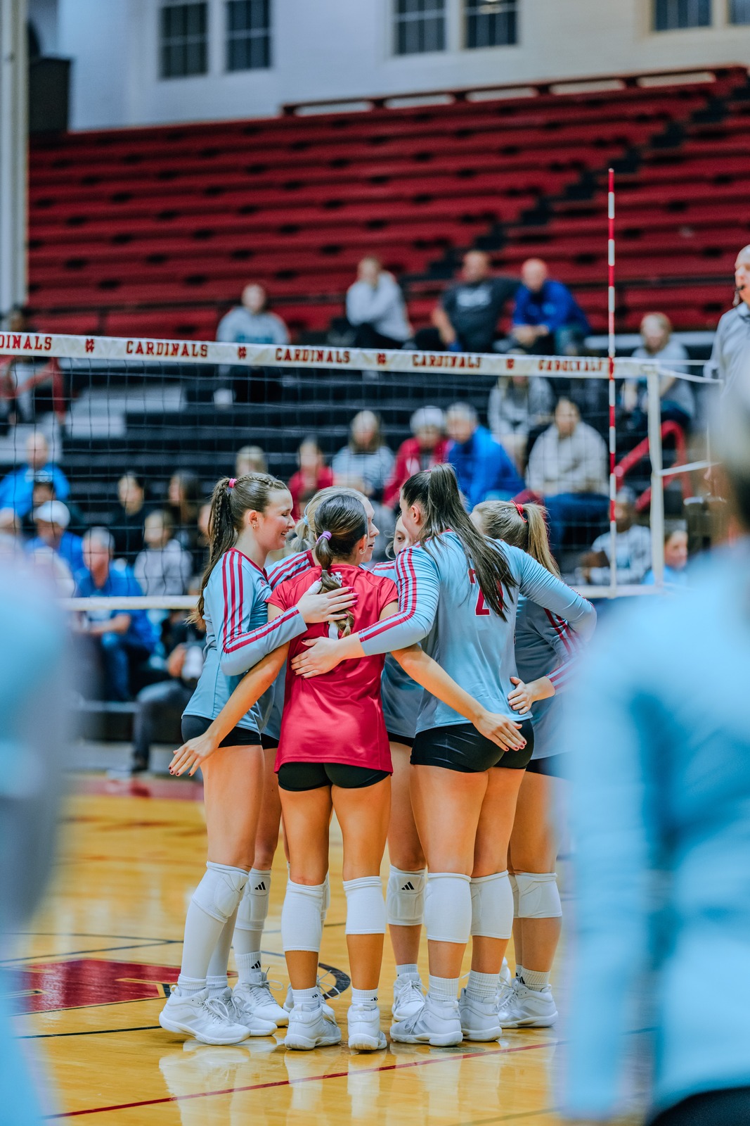 Players in light blue and red uniforms huddle together on a court.