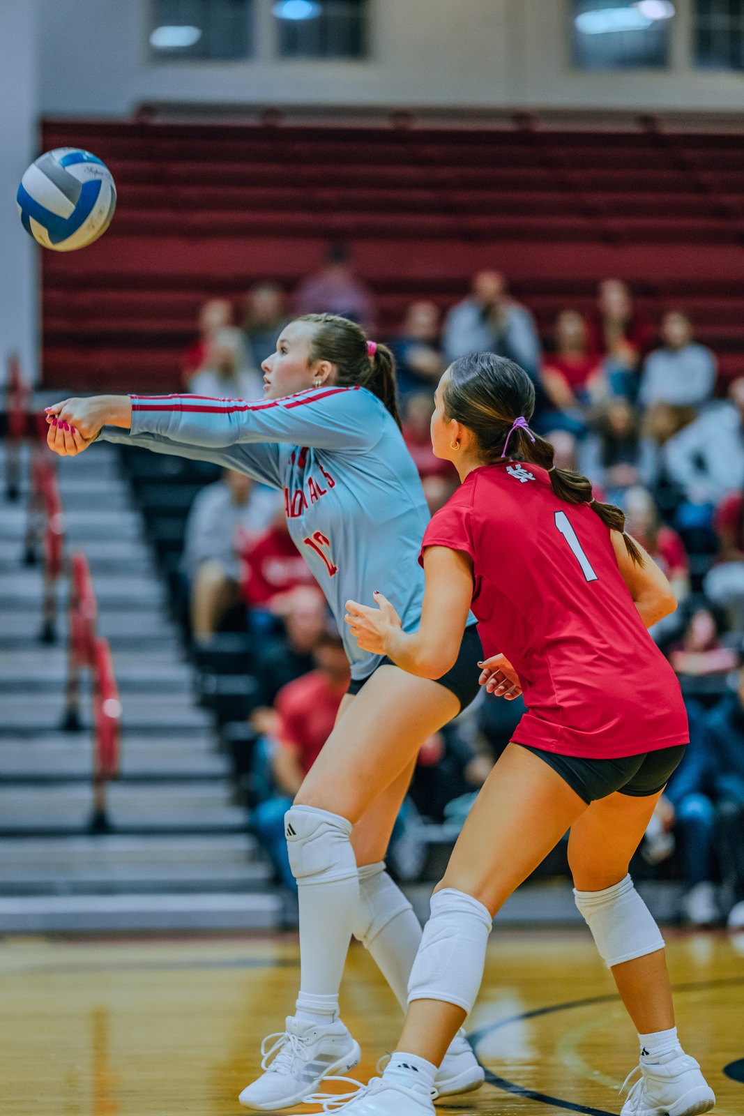 A player in a light blue uniform reaches for the ball while a player in a red uniform crouches.
