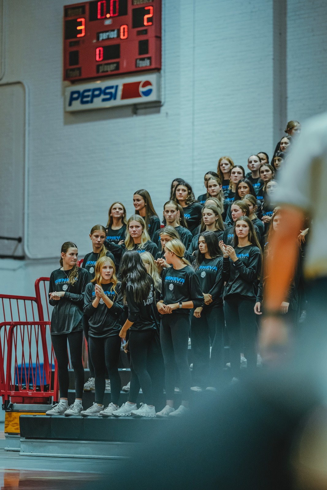 A group of players in black tops and leggings stand on bleachers.