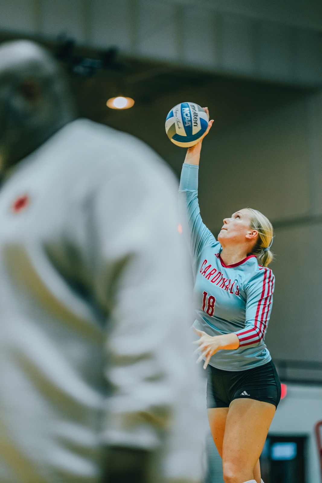 A player in a light blue jersey reaches overhead for the ball.