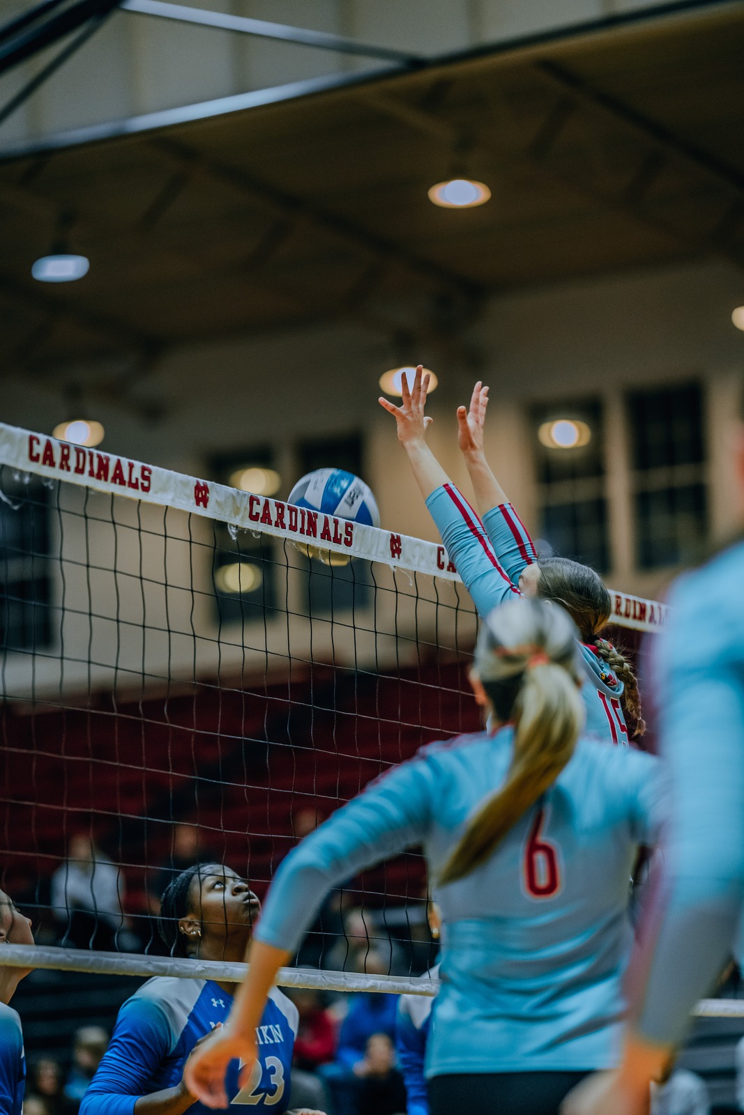 A player in a light blue uniform reaches overhead for the ball near the net.