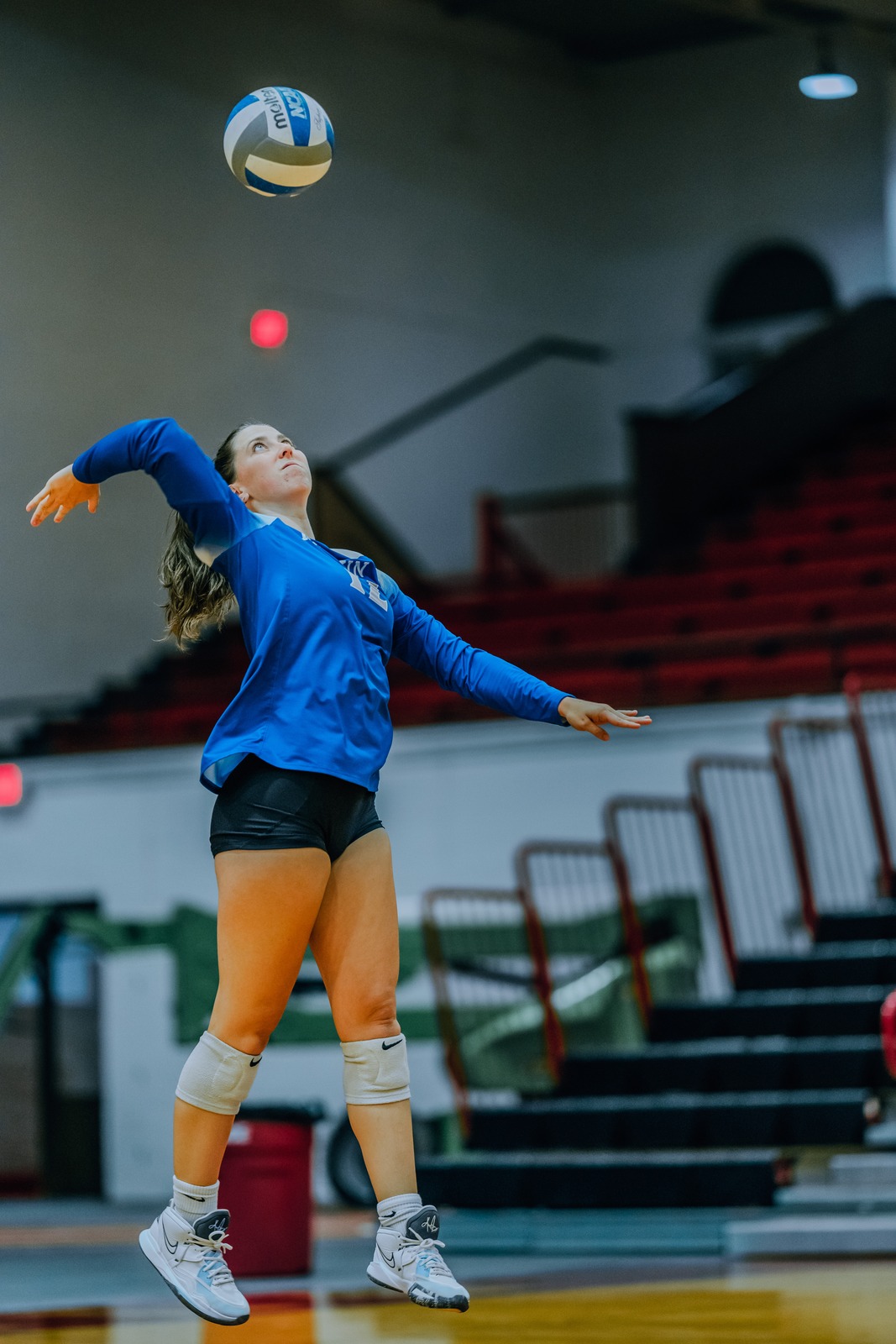 A player in blue jumps and reaches overhead for the ball.