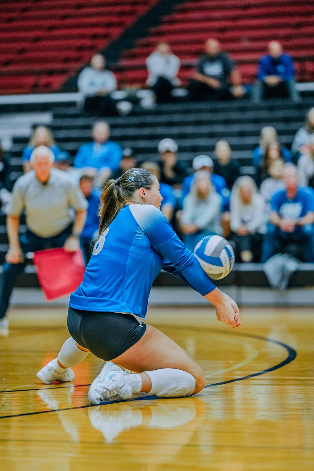 A player in a blue uniform crouches low and extends her arms toward the ball.