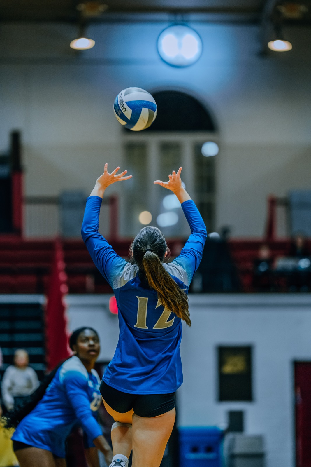 A player in blue reaches overhead for the ball.