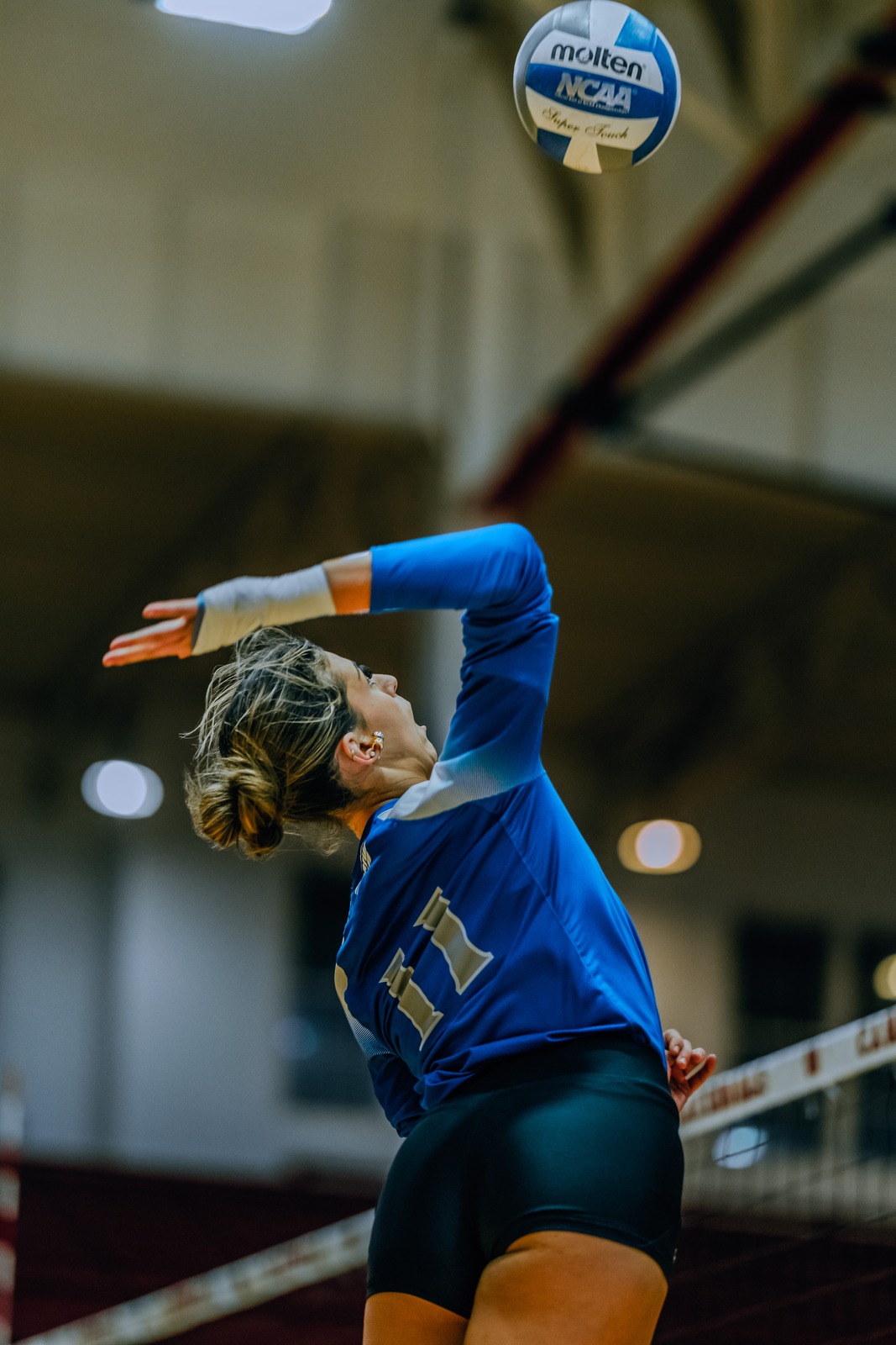 A player in a blue jersey reaches overhead for the ball.