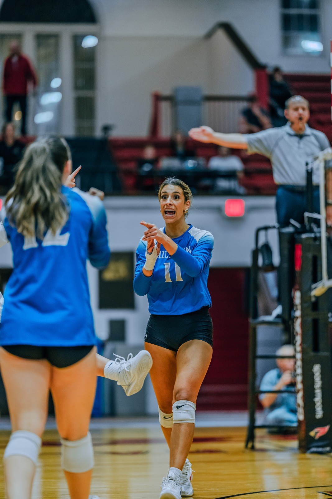 A Millikin player in a blue jersey points with both hands while looking forward.