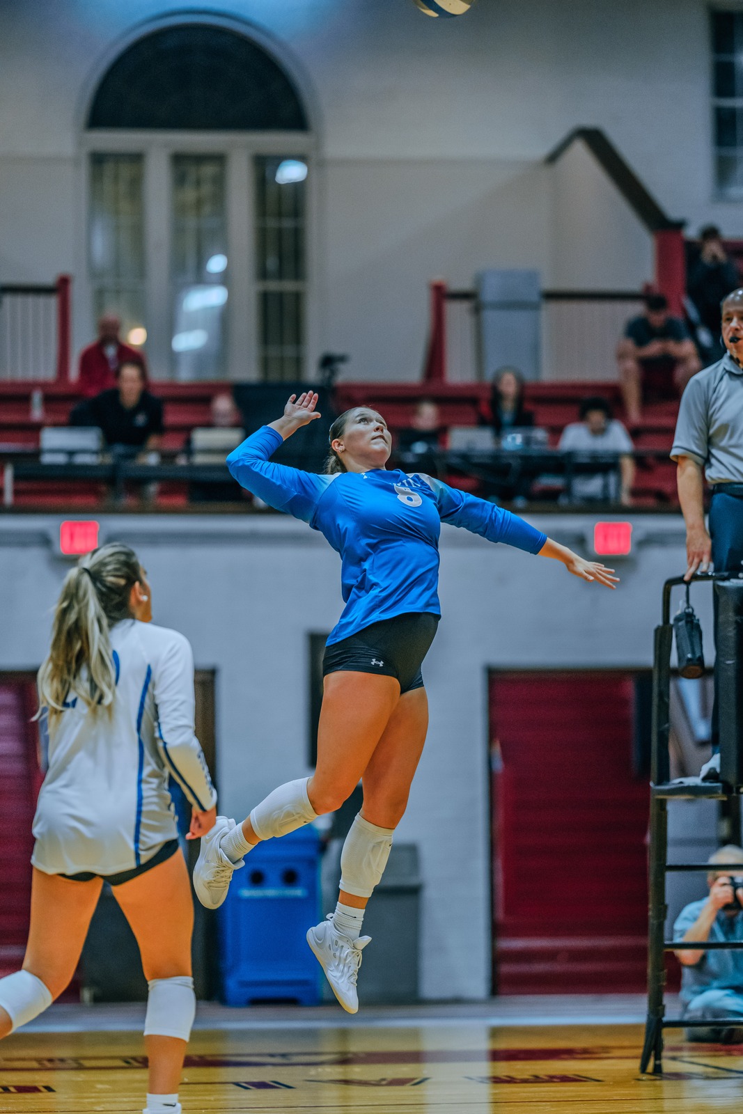 A player in blue jumps and reaches overhead for the ball.