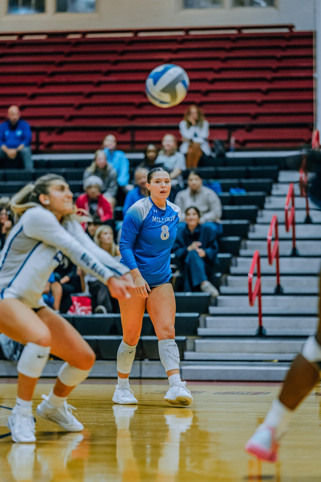 A Millikin player in blue reaches overhead for the ball.
