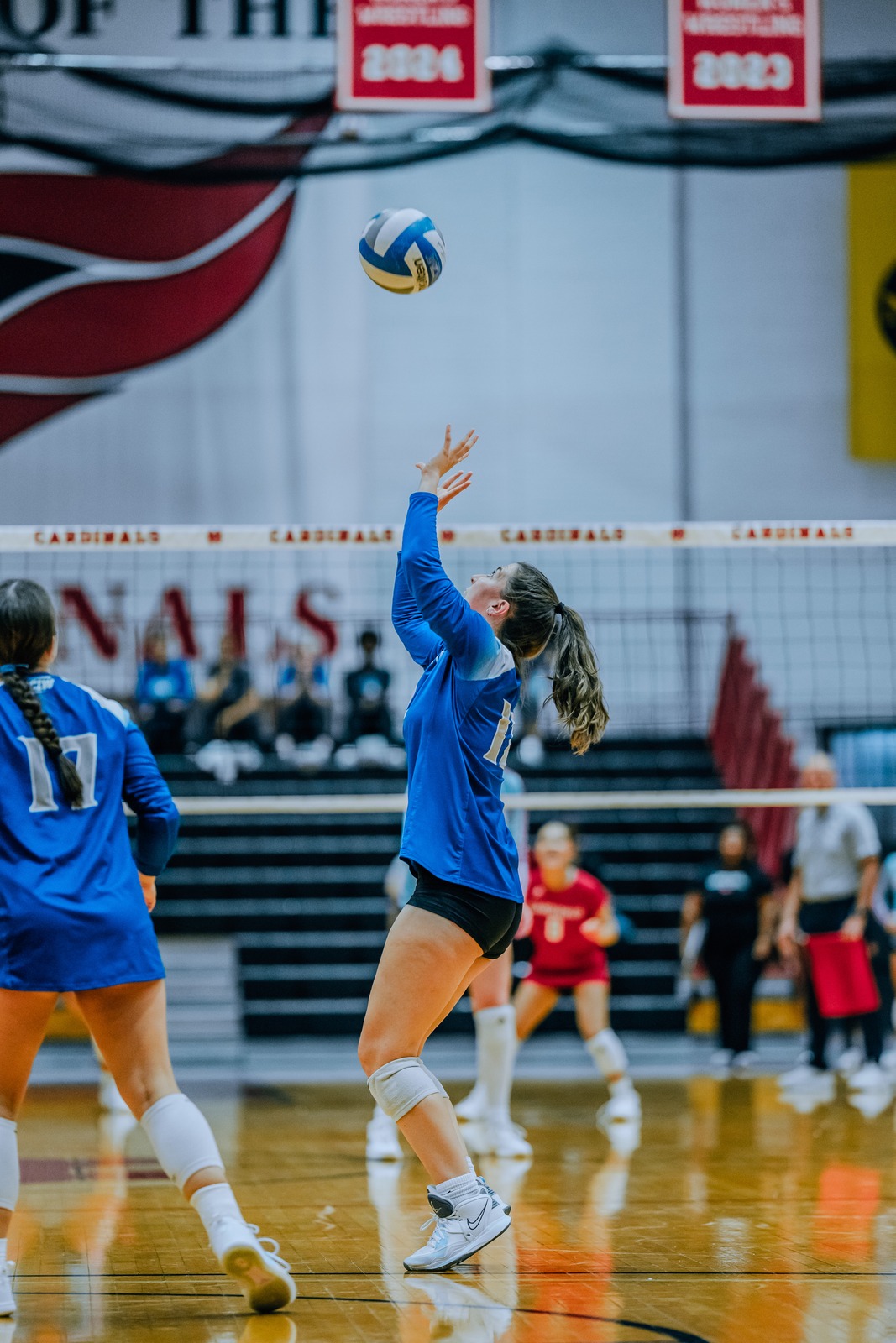 A player in a blue uniform reaches overhead for the ball.