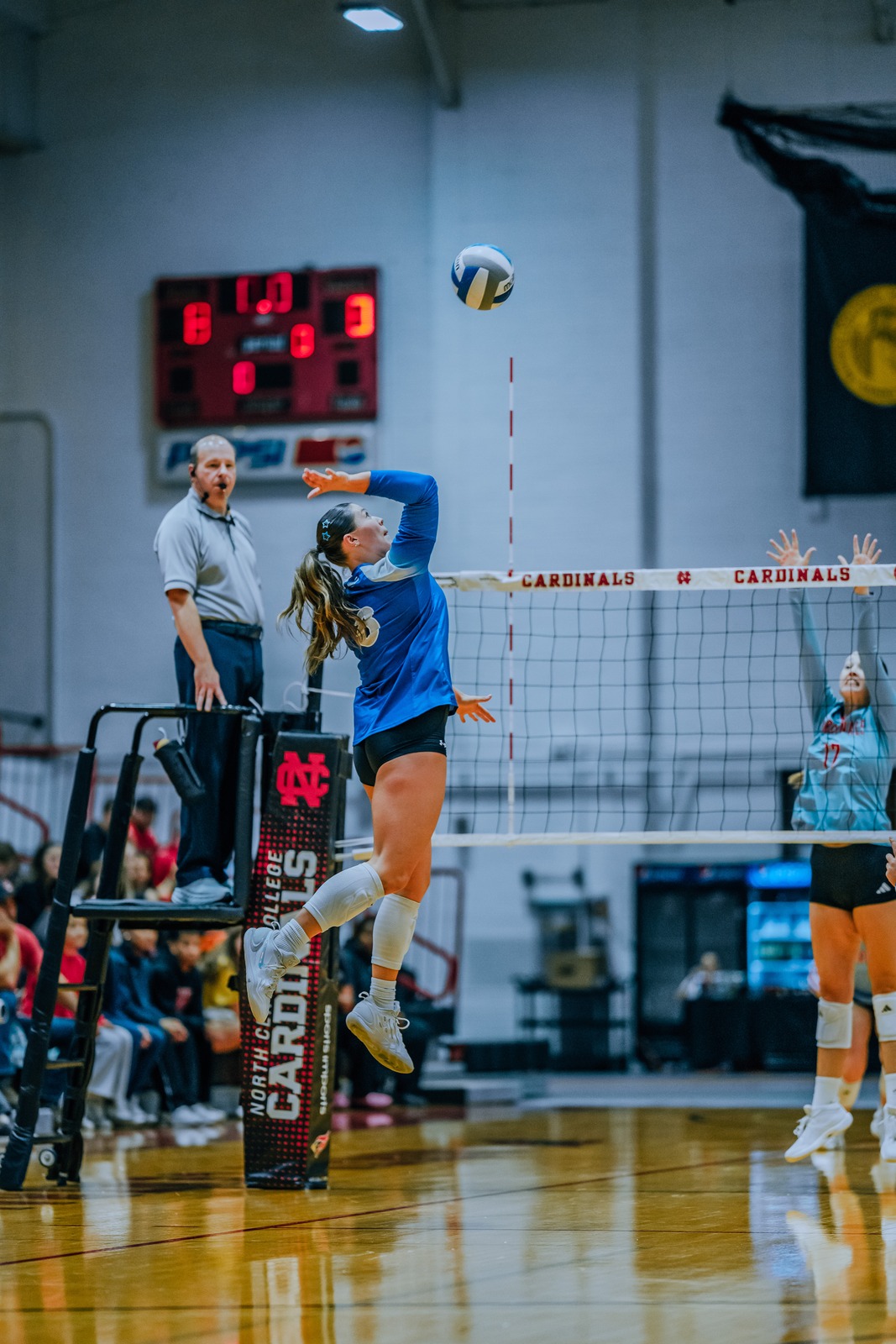 A player in blue jumps and reaches overhead for the ball.