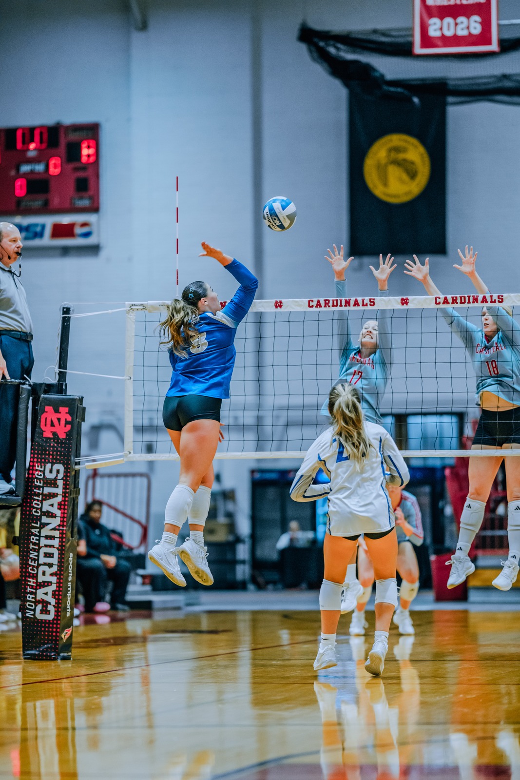 A player in blue jumps and swings at the ball over the net.
