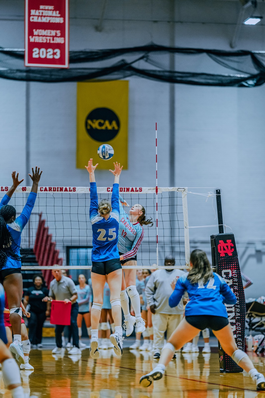 A player in blue jumps and reaches for the ball near the net.