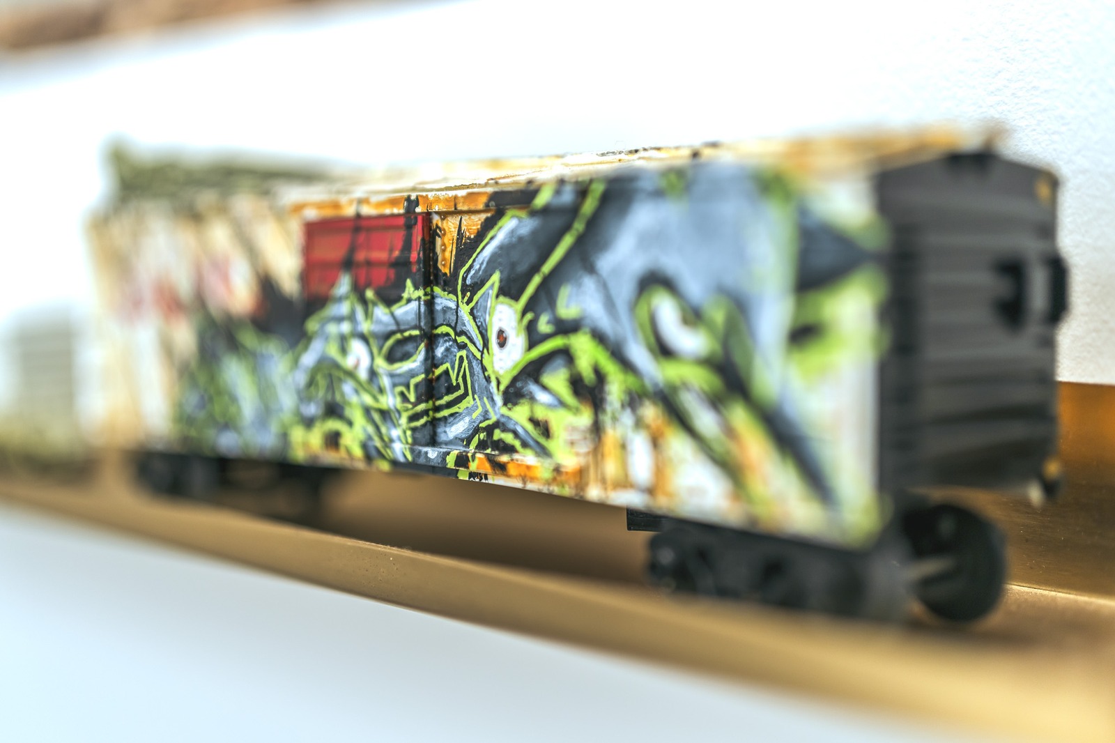 A miniature train car with graffiti art is displayed on a golden track.