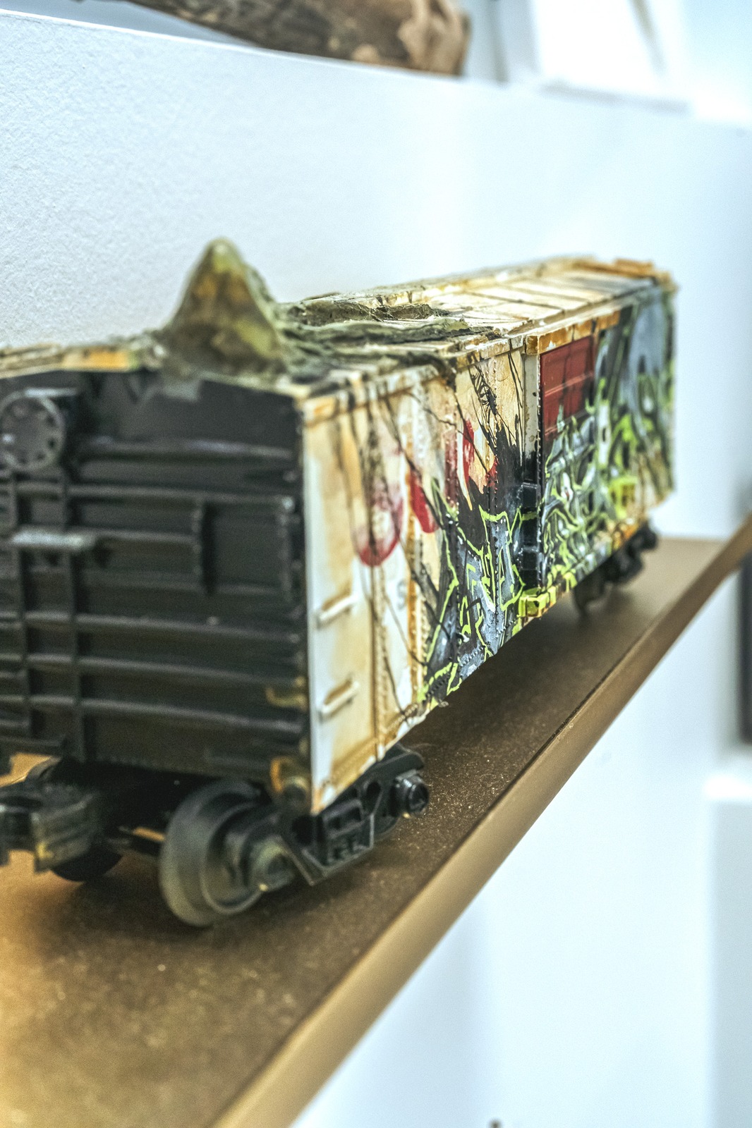 A miniature, graffiti-covered train car rests on a shelf.