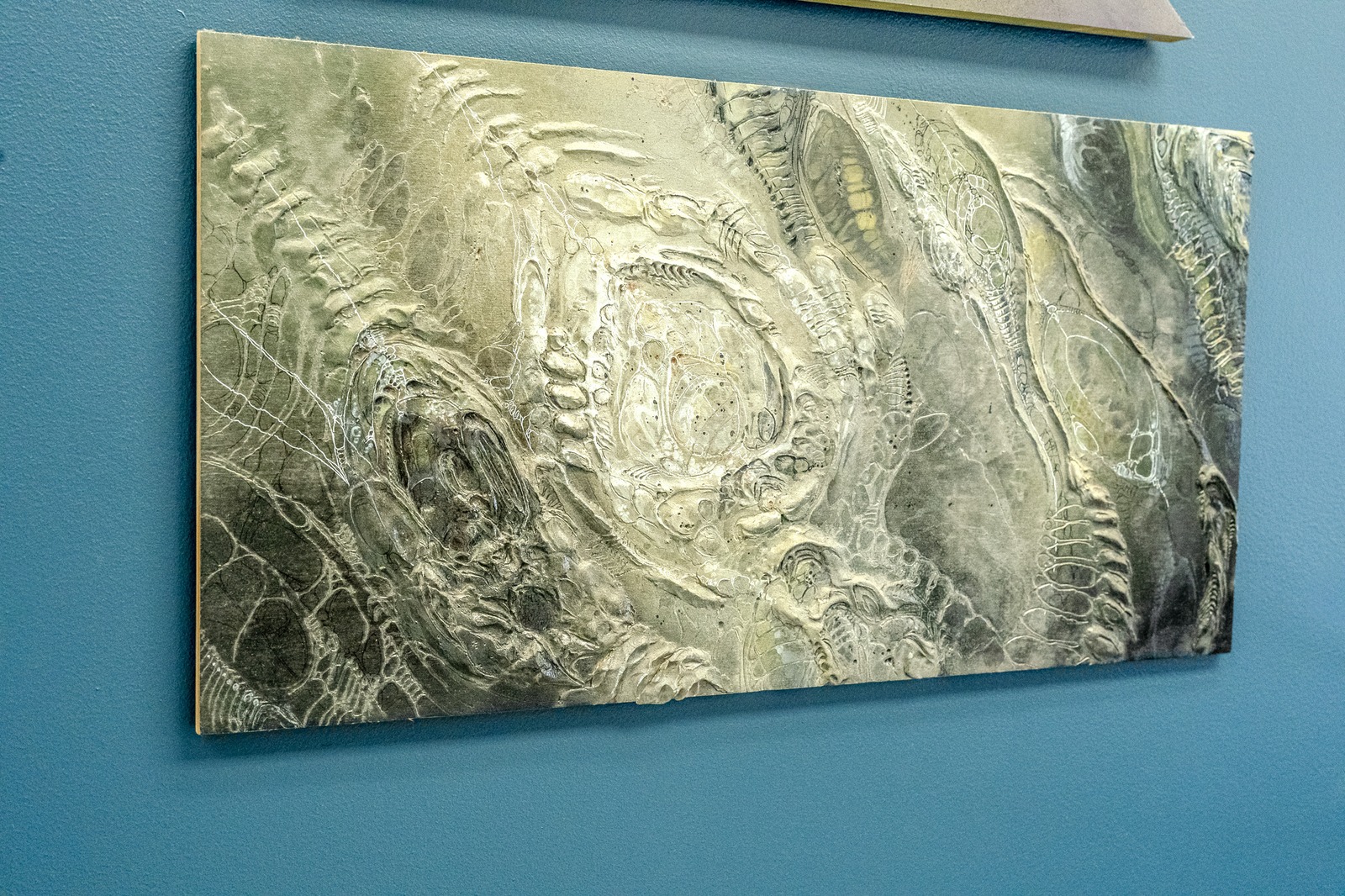 A textured artwork hangs on a blue wall.
