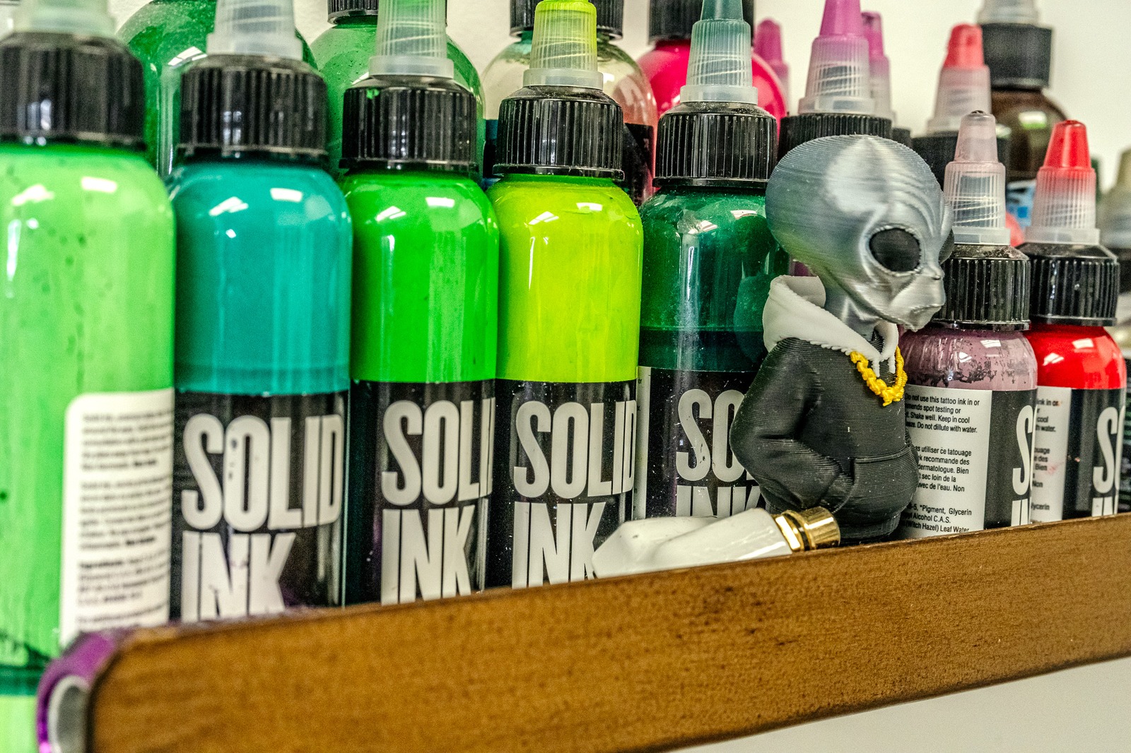 A small alien figurine stands among bottles of colorful liquid.