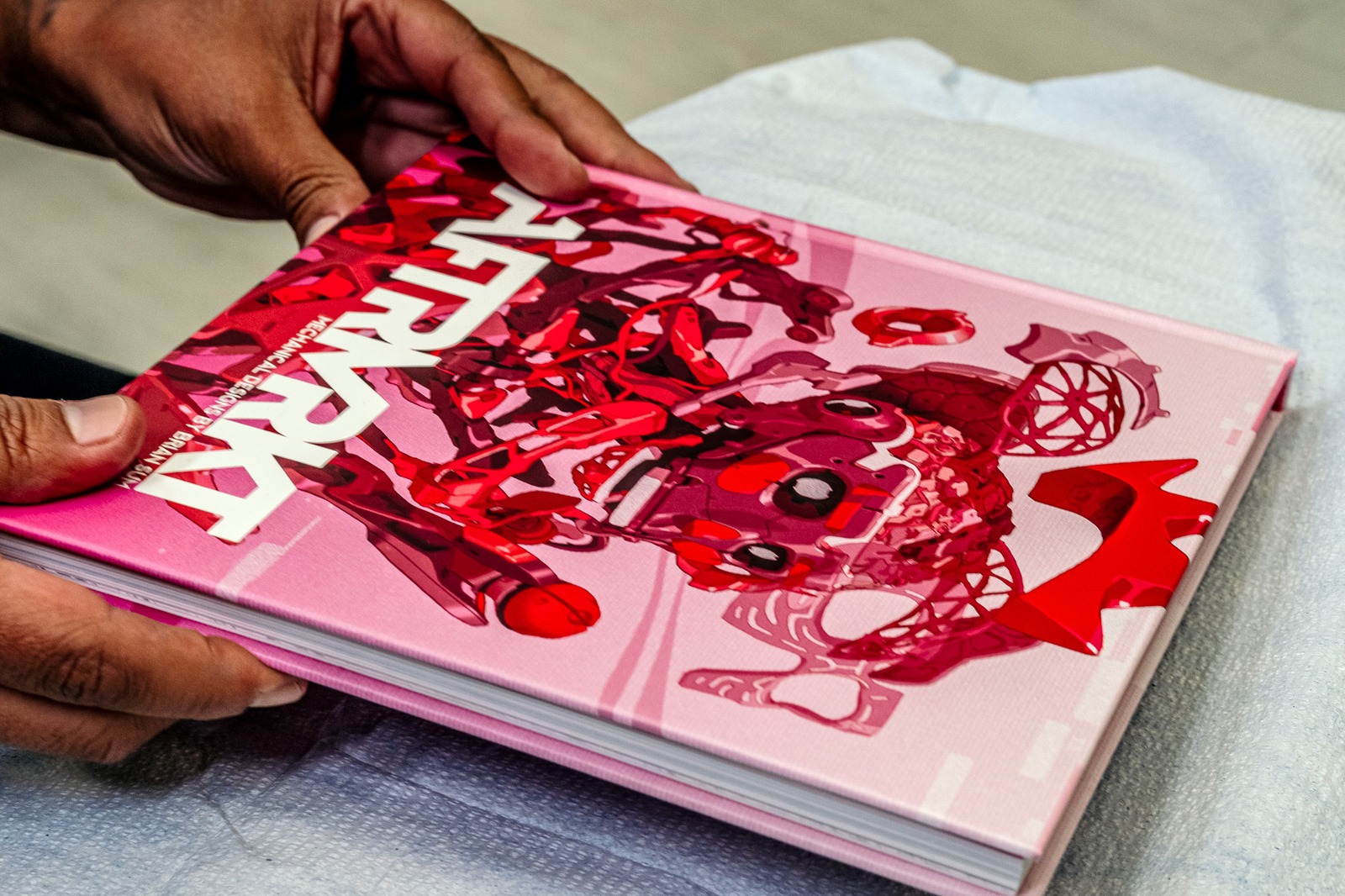 Hands hold a pink book with red abstract designs.