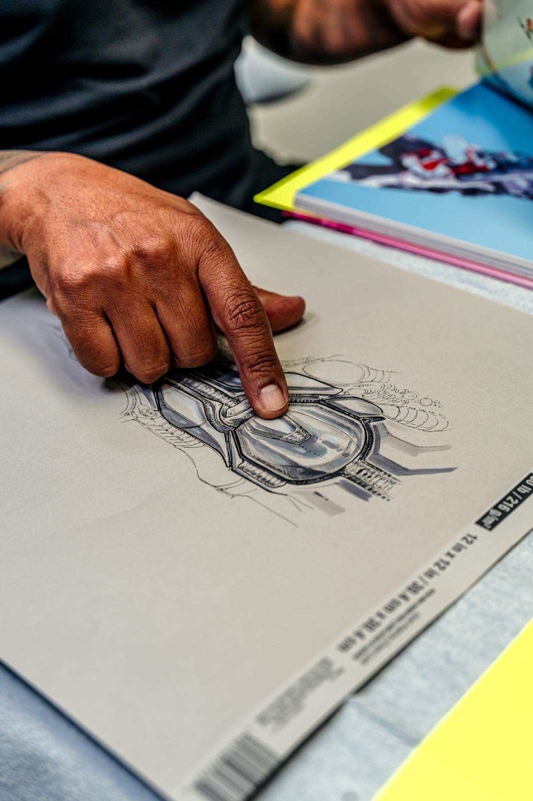 A hand points to a mechanical design drawn on paper.