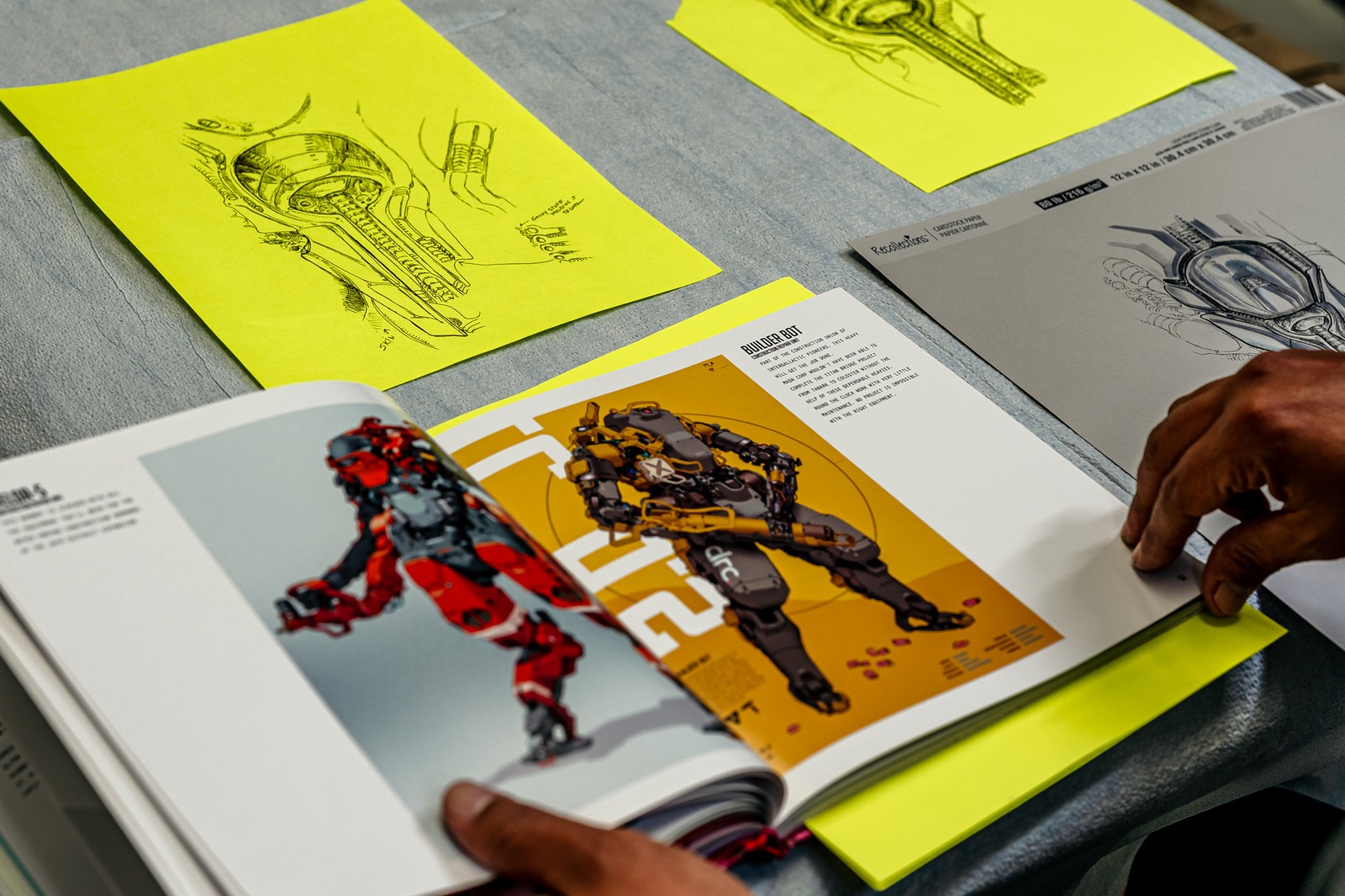 A hand turns a page in a book displaying a robot illustration.