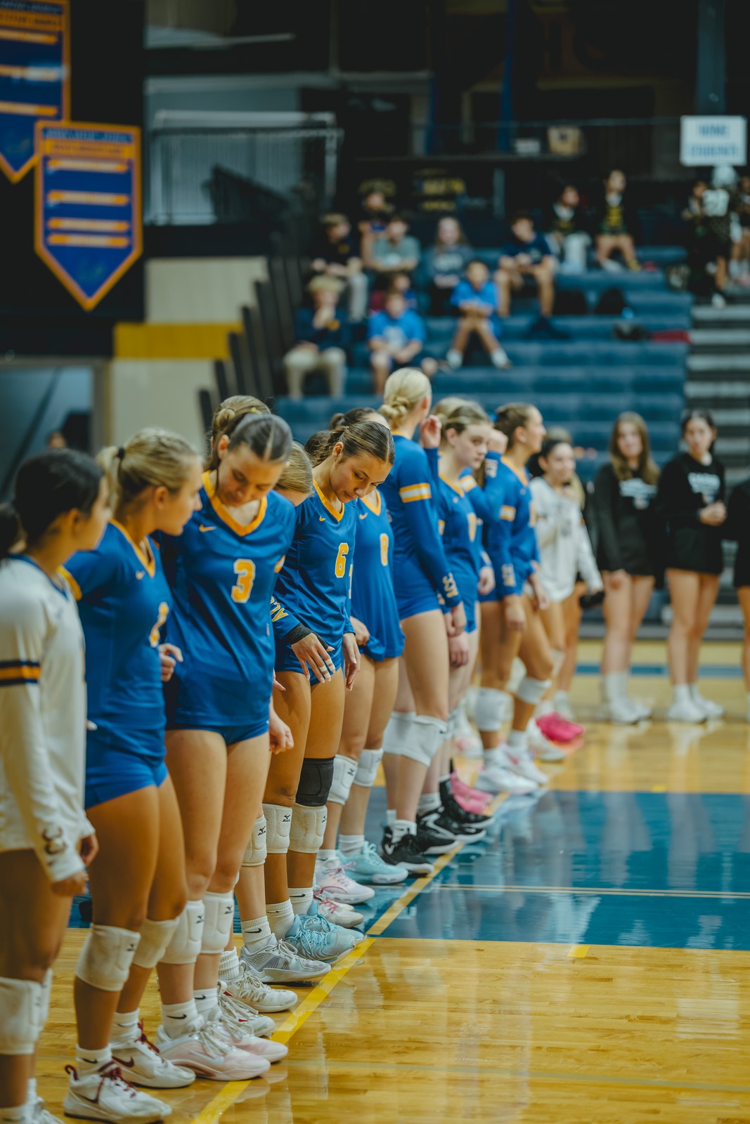 Players in blue uniforms stand in a line on a wooden court.