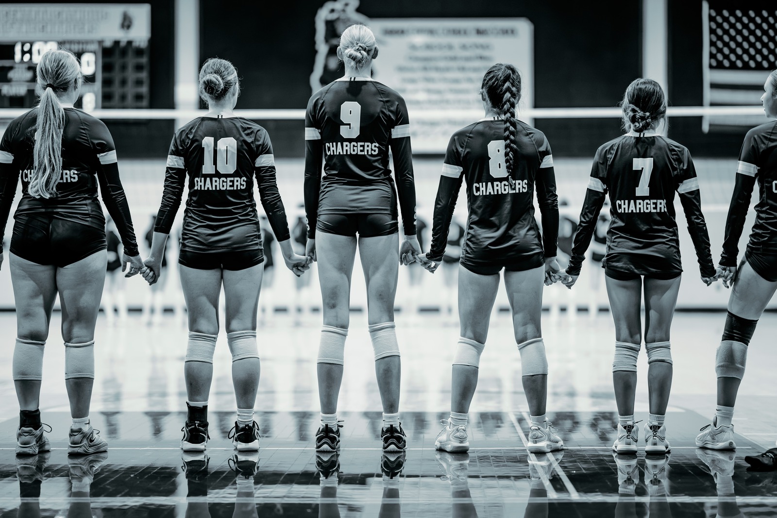 Players in black uniforms stand holding hands on a court.