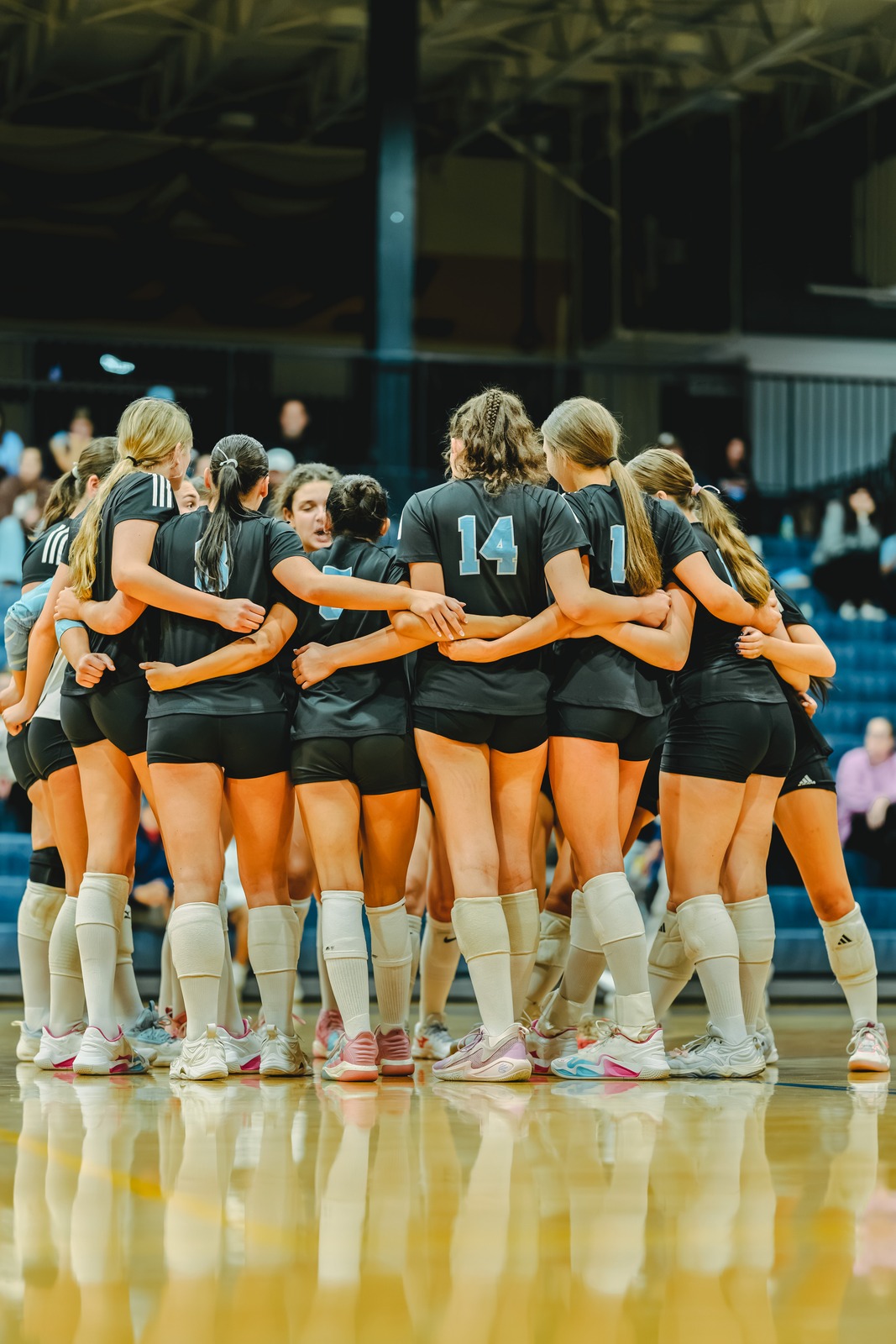Players in black uniforms huddle together on a court.