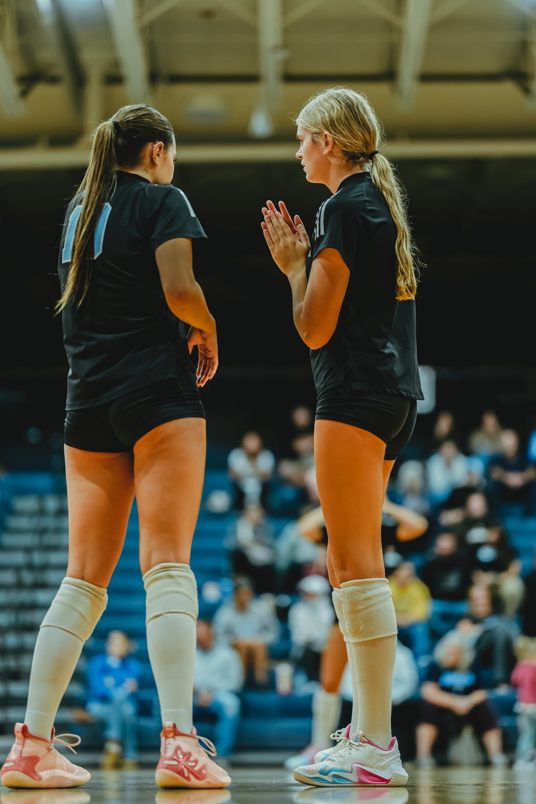A player in black claps her hands while standing next to a player in black.