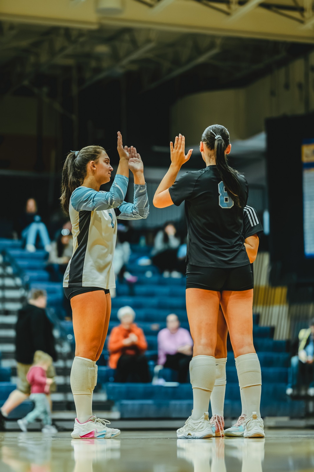 Two players in black and white uniforms high five on a court.