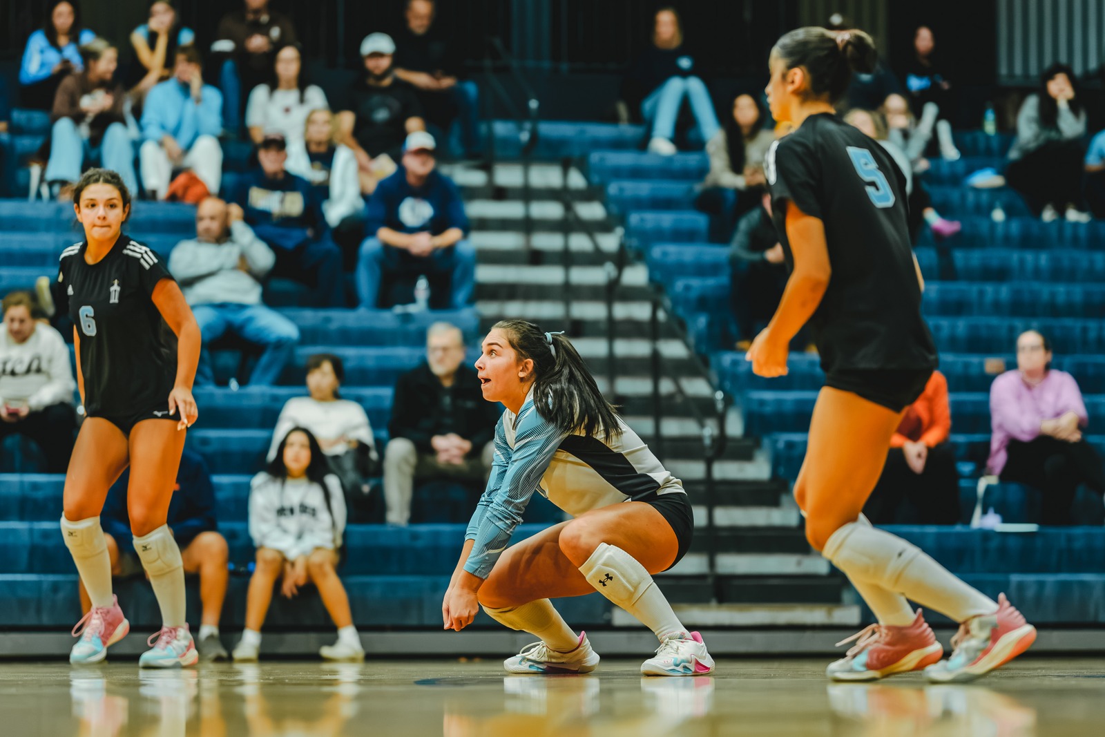 A player in light blue crouches low on the court.