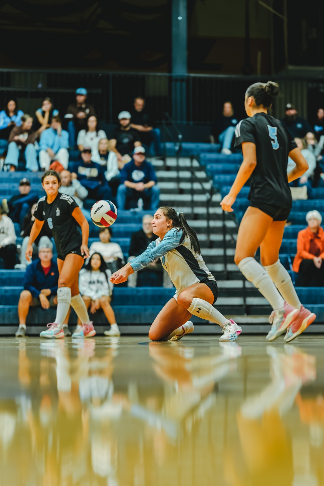 A player in a light blue and white uniform crouches low for the ball.