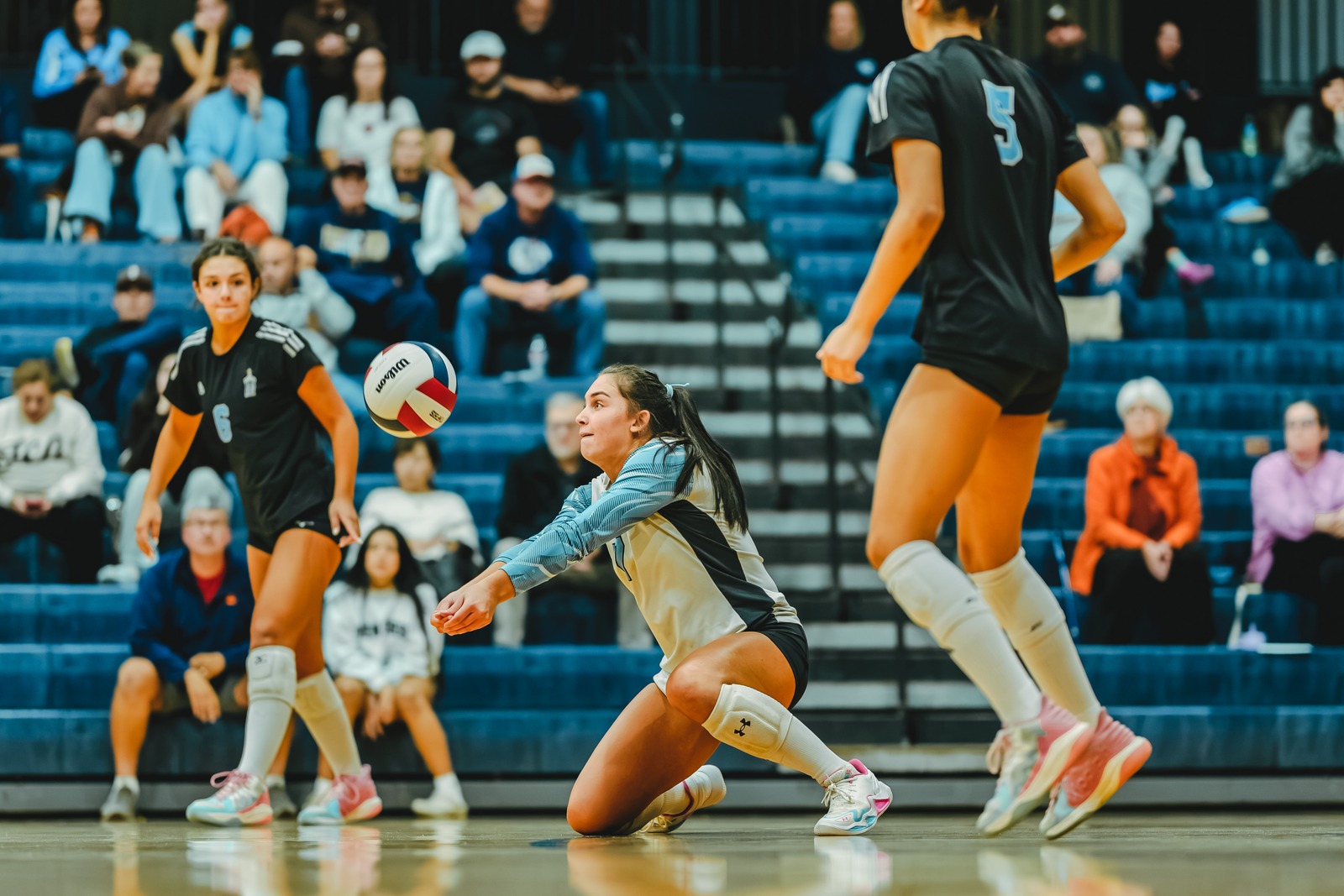 A player in a light blue uniform crouches low to the court, reaching for the ball.