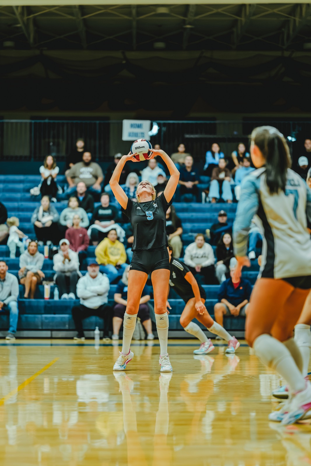 A player in black holds the ball overhead in a gym.