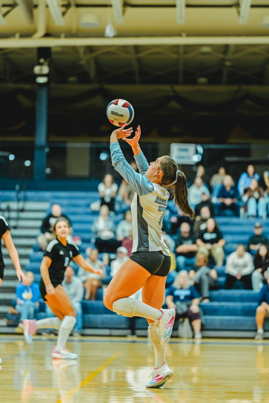 A player in a light blue and gray uniform reaches overhead for the ball.