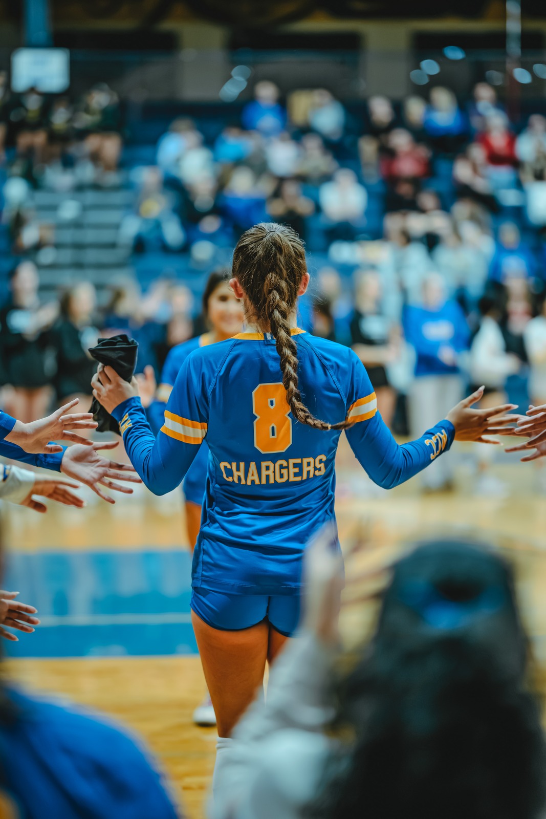 A player in a blue uniform with yellow trim reaches out to slap hands with teammates.