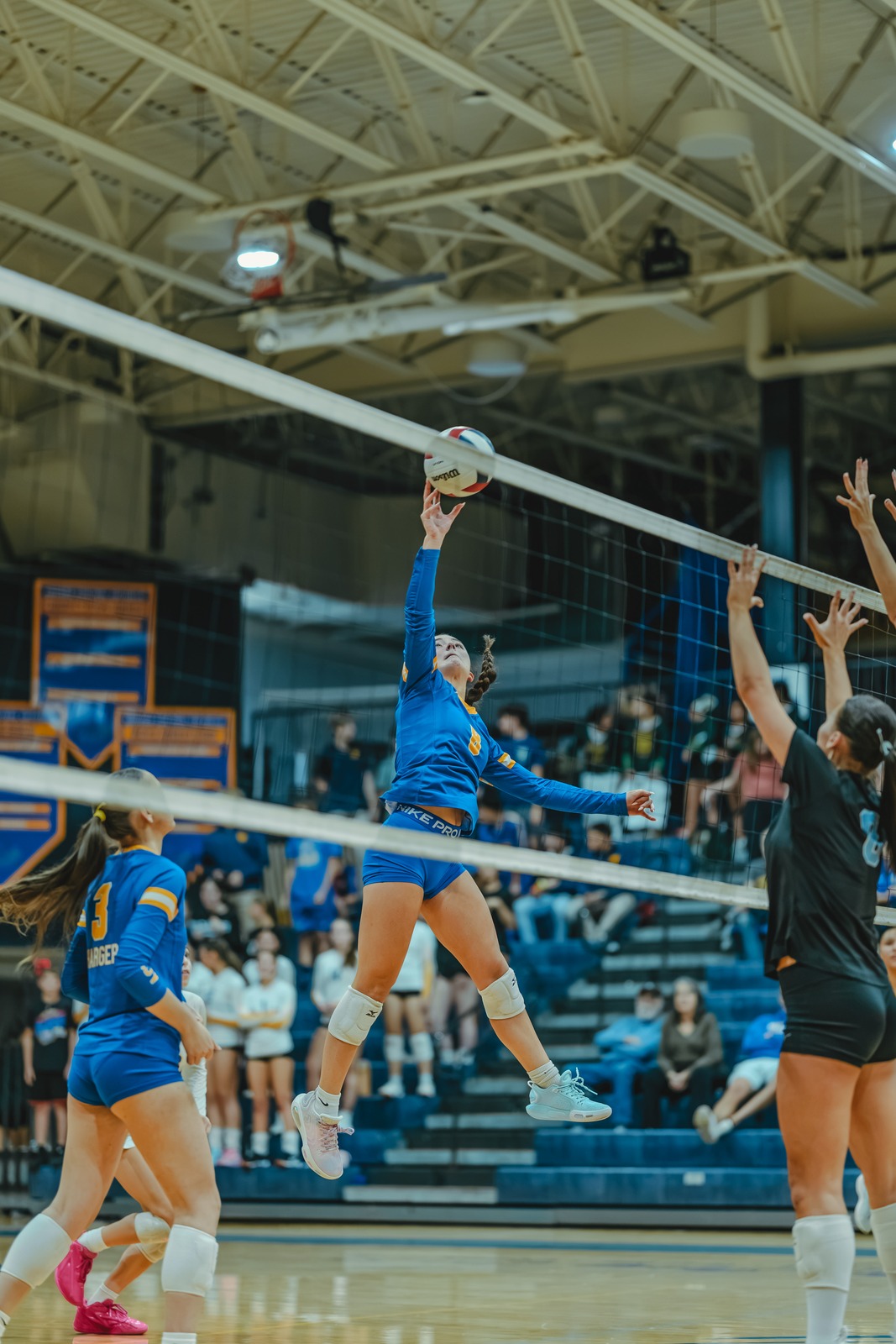 A player in blue reaches overhead for the ball while jumping.