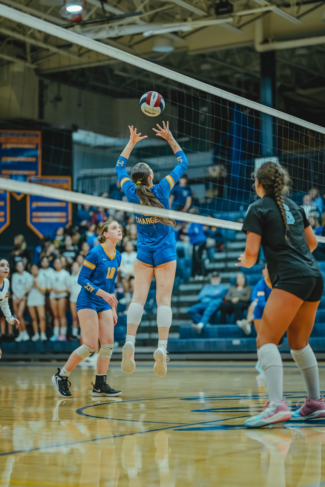 A player in blue jumps for the ball while another player in black watches.