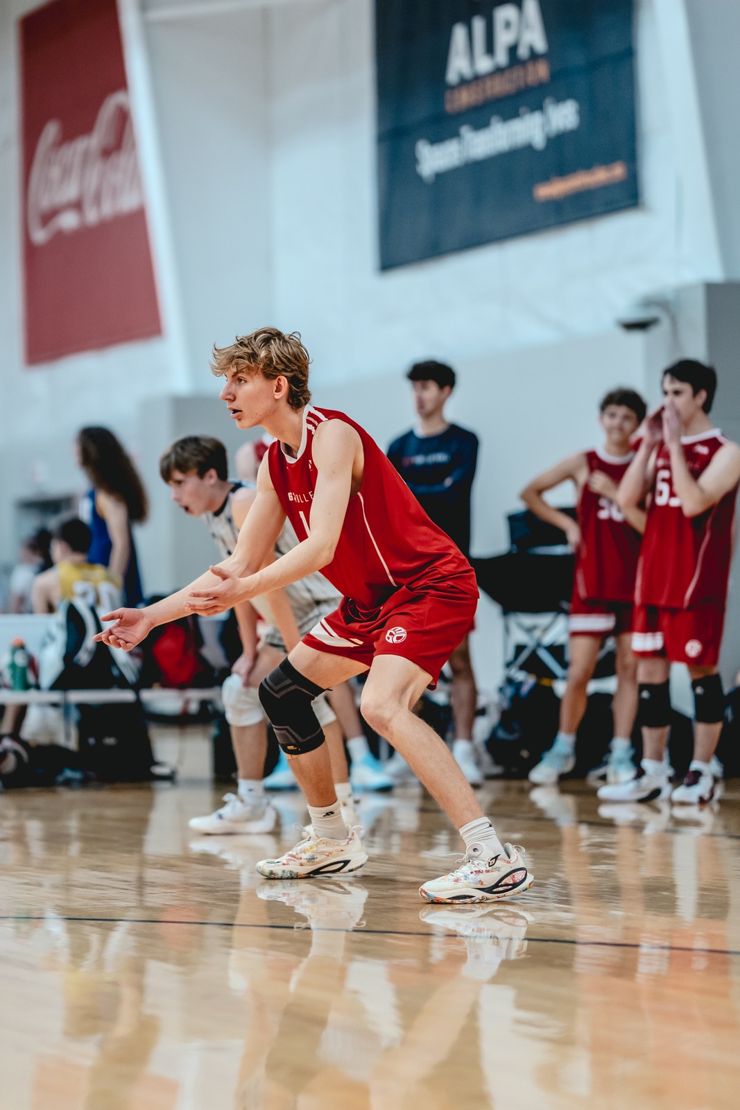 A player in a red top crouches low on a wooden court.