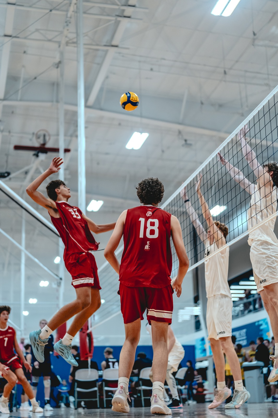 A player in red jumps near the net while players in white reach up.
