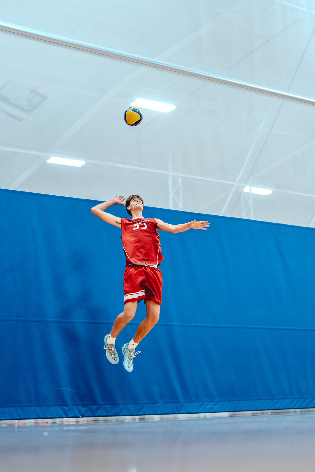A player in red jumps with arms extended, reaching for the ball.