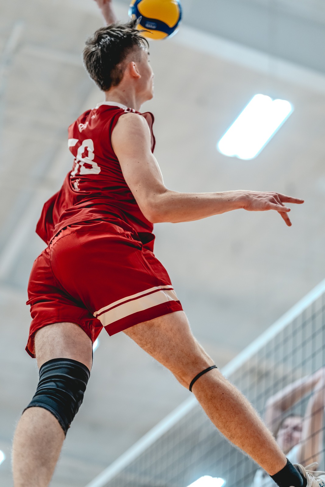 A player in red reaches up with a ball above their head.