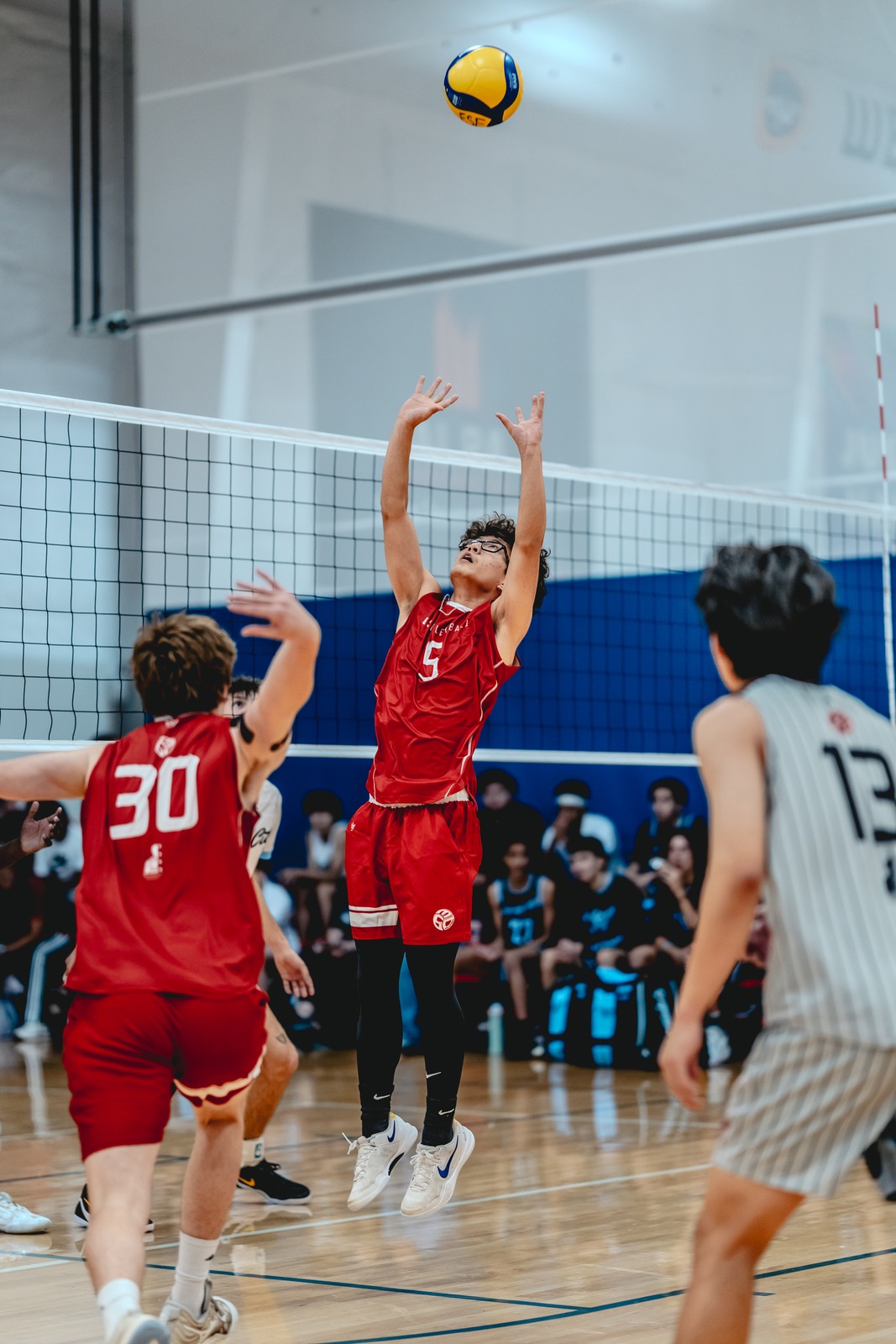 A player in red reaches overhead for the ball while in mid-air.