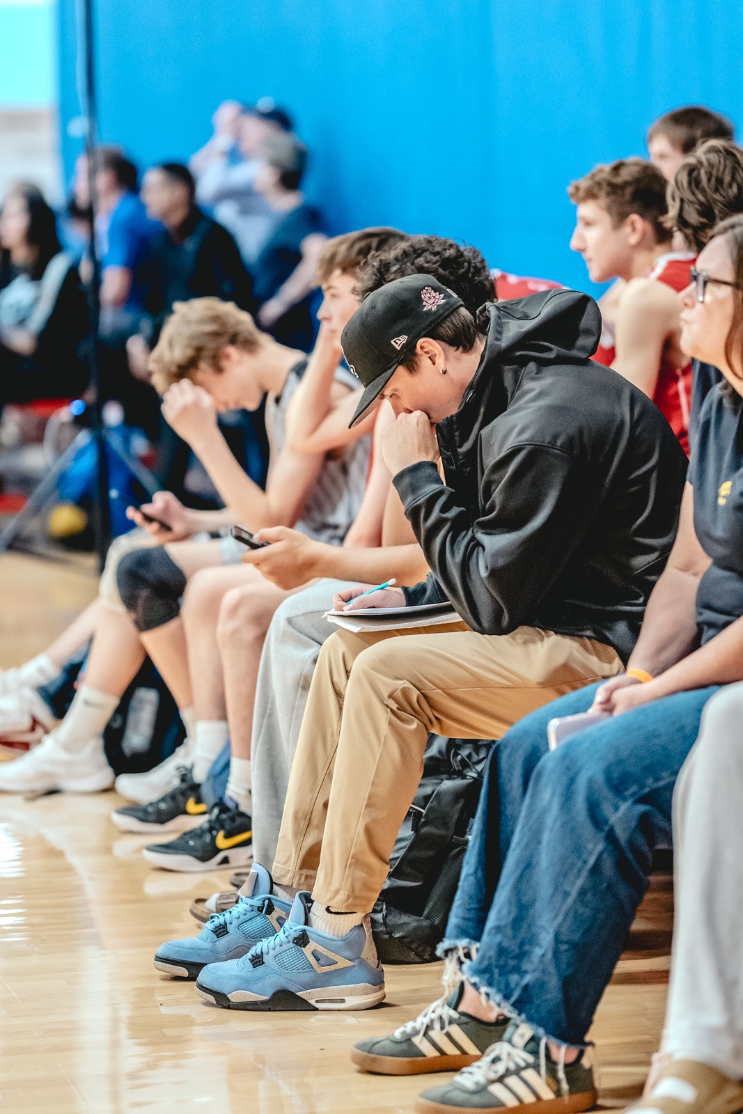 A player in a black hoodie writes in a notebook while other players sit on the bench.